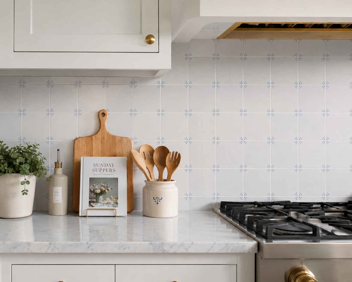 Akka Home Dutch Blue Delft peel and stick tiles as a kitchen backsplash behind a gas range, styled with marble countertop and cookware