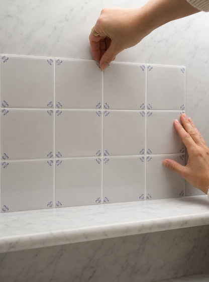 Hands pressing Akka Home Dutch Blue peel and stick Delft tiles onto a marble surface, no grout needed